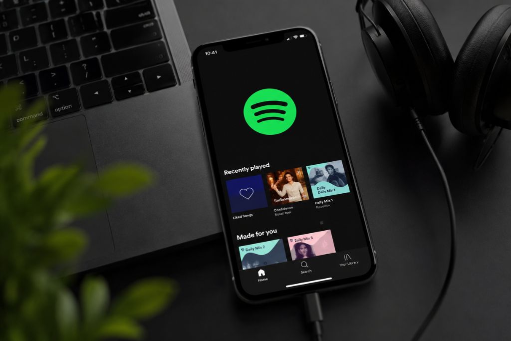 A mobile phone currently on the spotify app homepage beside a laptop